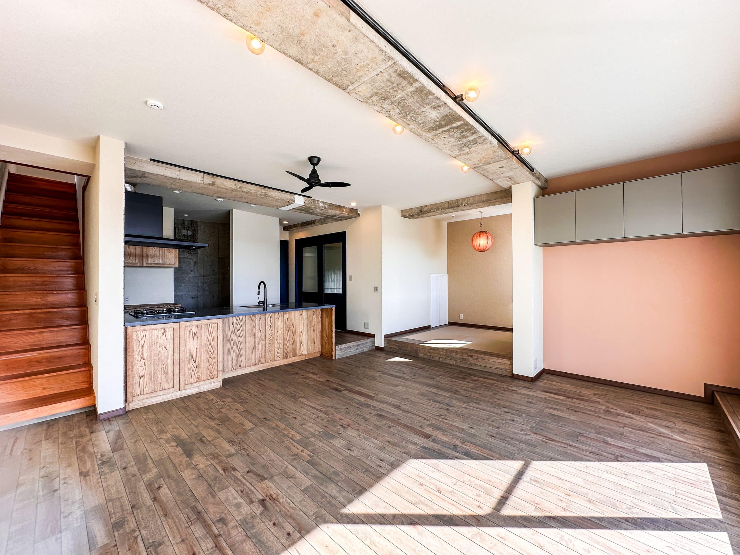 キッチン、小上がり、階段がひとつにつながるLDK全景。木の素材感とコンクリート梁のラフさが調和し、大きな窓から光が差し込む開放的な空間。